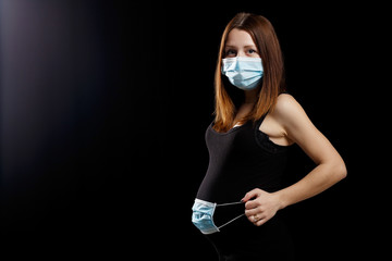 Fototapeta na wymiar pregnant woman in a black dress with dark hair with a medical mask against coronavirus pandemic infection COVID-19