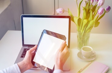 Close-up of tablet with blank screen in hands of young woman sitting at white table and touching...