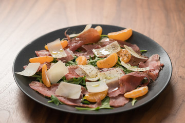 Salad with prosciutto, tangerines and vintage cheese on walnut table