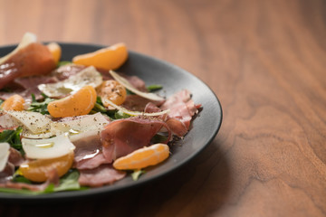 Salad with prosciutto, tangerines and vintage cheese on walnut table with copy space
