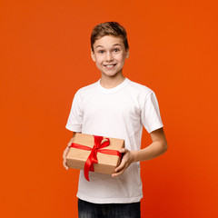 Cheerful teen boy enjoying gift box, orange studio background