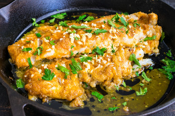 Baked Cod with Lemon and Garlic: Breaded whitefish fillet topped with chopped garlic and parsley in a cast iron skillet
