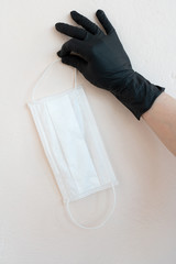 COVID-19, pandemic, hand in a black glove on a light background holding a white medical mask