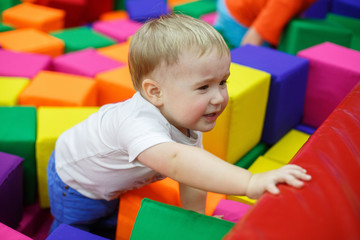 Fototapeta na wymiar smiling child in playroom. funny baby boy in a pool with colorful soft toy cubes. family rest in the children's center. portrait a little boy have fun in playing room close up. happy childhood concept