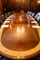 Large wooden table in a board room with wood panelling, set up for a meeting