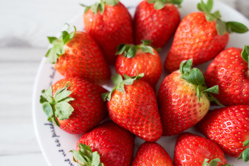 Fototapeta na wymiar Fresh strawberries on a white plate on a soft wooden base