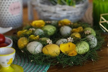 Close-up of painted green, yellow and white spotted eggs decorated in green wreath with decorative wooden flowers on table.