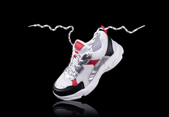 Obraz premium White sneakers isolated on a black background with a reflection at the bottom, with floating laces