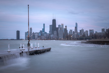 Fantastic cityscape panoramic skyline view of Chicago from Fullerton Avenue during a windy day with water cascading over a concrete pier at night just after sunset as lights begin to turn on in city.