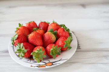 Fresh strawberries on a white plate on a soft wooden base