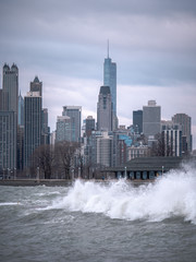 Chicago skyline view with waves crashing into the tiered shoreline and cascading back into the...