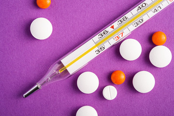 Pills, tablets and analog thermometer on violet purple background, healthcare medical concept,...
