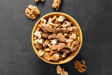 Walnuts in wooden bowl, isolated over dark background, top view with copy space.