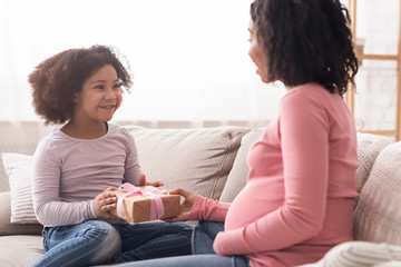 Little black daughter giving gift to her surprised pregnant mom