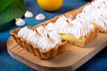 Lemon tart with caramelized meringue cut into pieces on the blue wooden table