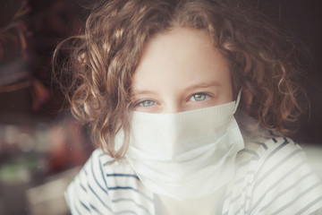 girl in a mask behind glass coronavirus window