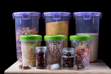 Assortment of groats and spices in plastic and glass jars on the wooden kitchen shelf. Concept of storage of non-perishable products
