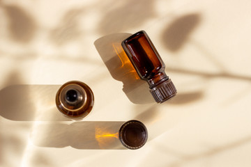 Glass cosmetic bottles with a dropper on a beige background with bright sunlight and hard shadows....