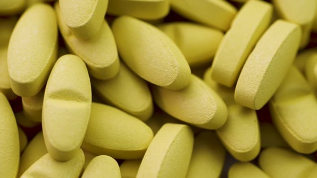 Bright yellow antipyretic tablets lie together and rotate closeup