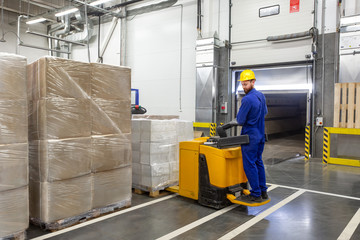 Young forklift driver loading goods in a warehouse with gate