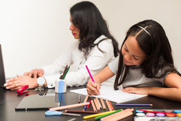 Latin mother and daughter working at home. Little girl doing homework on the desk while her mother...