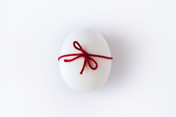 White egg with red wool thread ribbon on white background