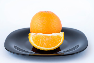 Juicy tasty orange and orange slice on black plate on white background isolated
