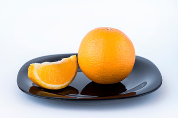 Juicy tasty orange and orange slice on black plate on white background isolated