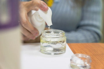 woman pouring oil into cream in glass jar