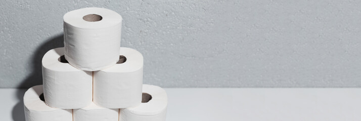 Panoramic banner with copy space, close-up of toilet paper rolls on white table, background of textured wall grey of color.