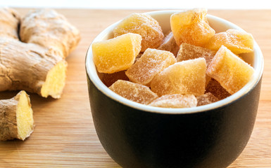 close up of home made ginger candies and fresh ginger on wooden table.
