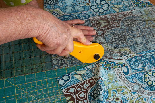 Closeup Of A Woman`s Hands Using A Rotary Cutter To Cut Quilting Fabric