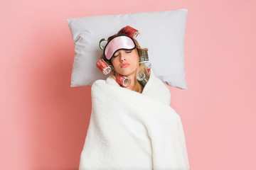 Housewife in curlers and mask, sleeps with blanket and pillow