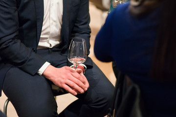 Man in suite sitting holding a glass of white wine, body parts photographed on a wine tasting event.