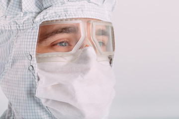 Portrait of a male doctor of European appearance in a medical mask, protective glasses and chemical suit.
