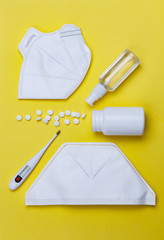 Sanitizer, protective mask and pills on a yellow background