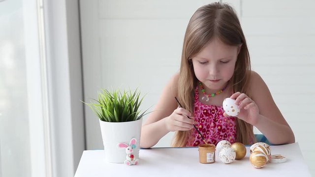 Little girl painting eggs with gold paint. Happy Easter. Easter eggs 
