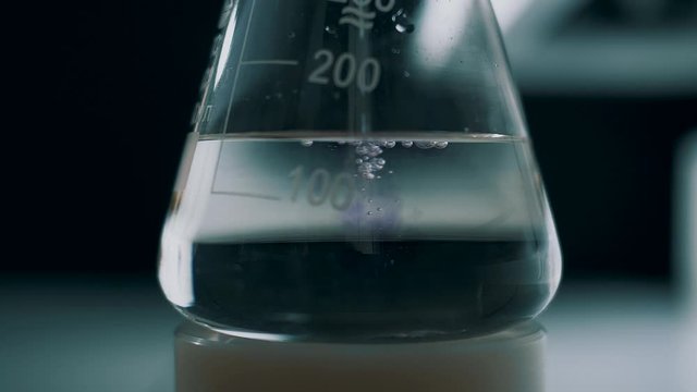 Laboratory assistant mixes reagents in a test tube flask for analysis. Slow motion