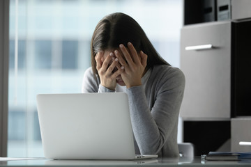 Unhappy young woman sit at desk in office distracted from computer work suffer from depression or...