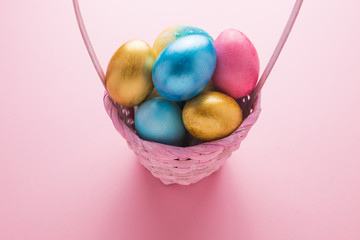 Multi-colored Easter eggs in a basket on a pink isolated background. Easter is a bright holiday.