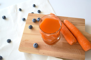 Carrot juice in a glass and blueberries on a white tablecloth. Carrots on a wooden board