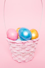 Multi-colored Easter eggs in a basket on a pink isolated background. Easter is a bright holiday.