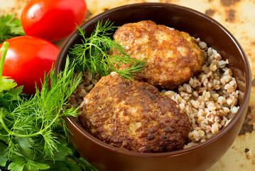 Homemade cutlets with tomatoes and salad in a bowl on a rusty background.