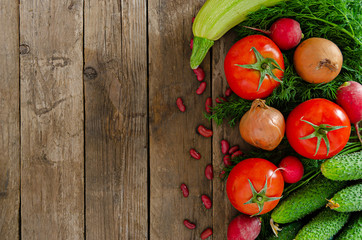 Fresh rustic vegetables on an old wooden table - tomatoes, cucumbers, onions, dill, beans, radishes.