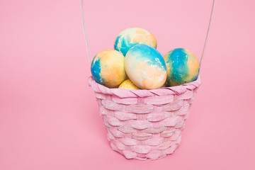 Multi-colored Easter eggs in a basket on a pink isolated background. Easter is a bright holiday.