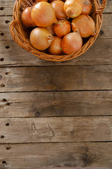 Wicker basket with onions on an old wooden table.