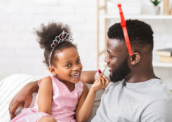 Adorable black baby girl putting lipstick on her dad lips