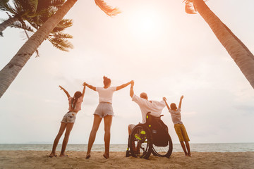 Disabled man in a wheelchair with his family on the beach. Silhouettes at sunset