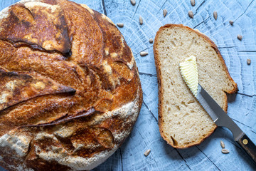 Top view of artisan bread loaf and a slice with butter surrounding by some sunflower seeds on wooden background