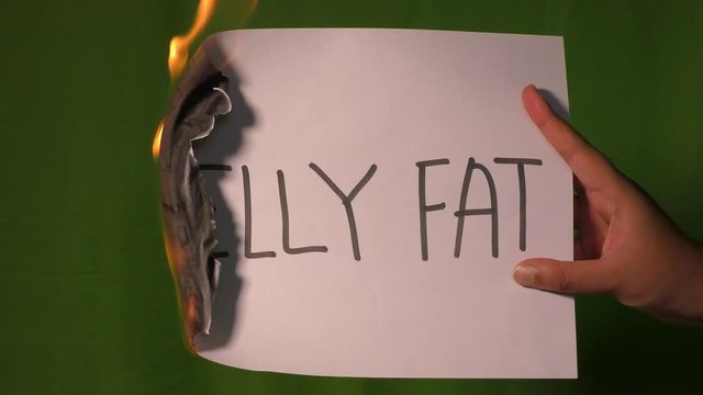 A hand holds the burning paper with belly fat word on it.